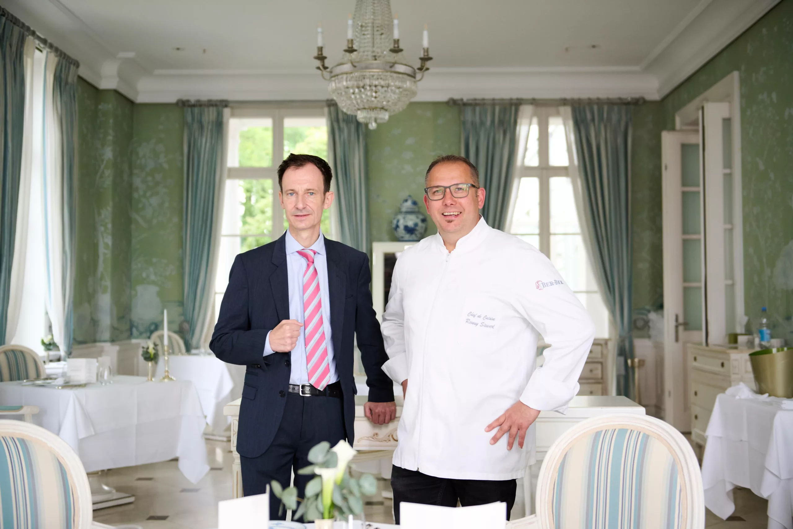 Sternekoch Ronny Siewert und Restaurantleiter Norman Rex begrüßen Gäste in einem elegant, warm beleuchteten Restaurant.